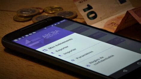 Photo d'un smartphone avec l'application Android Abcba ouverte au milieu de pièces de monnaie et d'un billet.