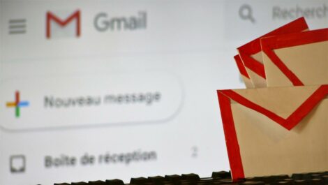 Photo d'envellopes papier aux couleurs de Gmail posées sur un clavier d'ordinateur avec site Gmail en arrière plan.