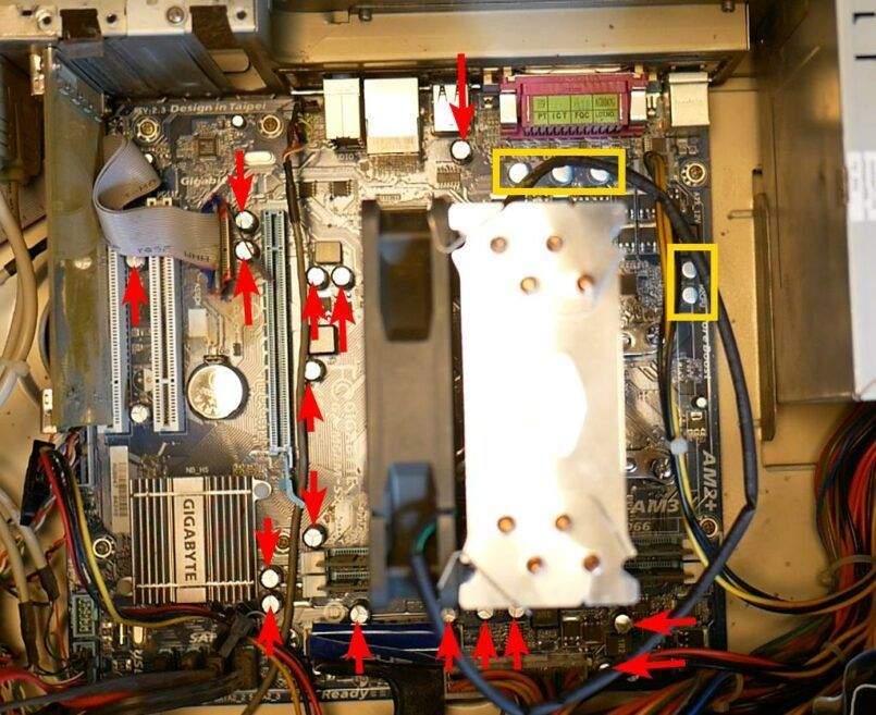 Photo d'une carte mère de PC avec des flèches rouges sur les condensateurs à vérifier